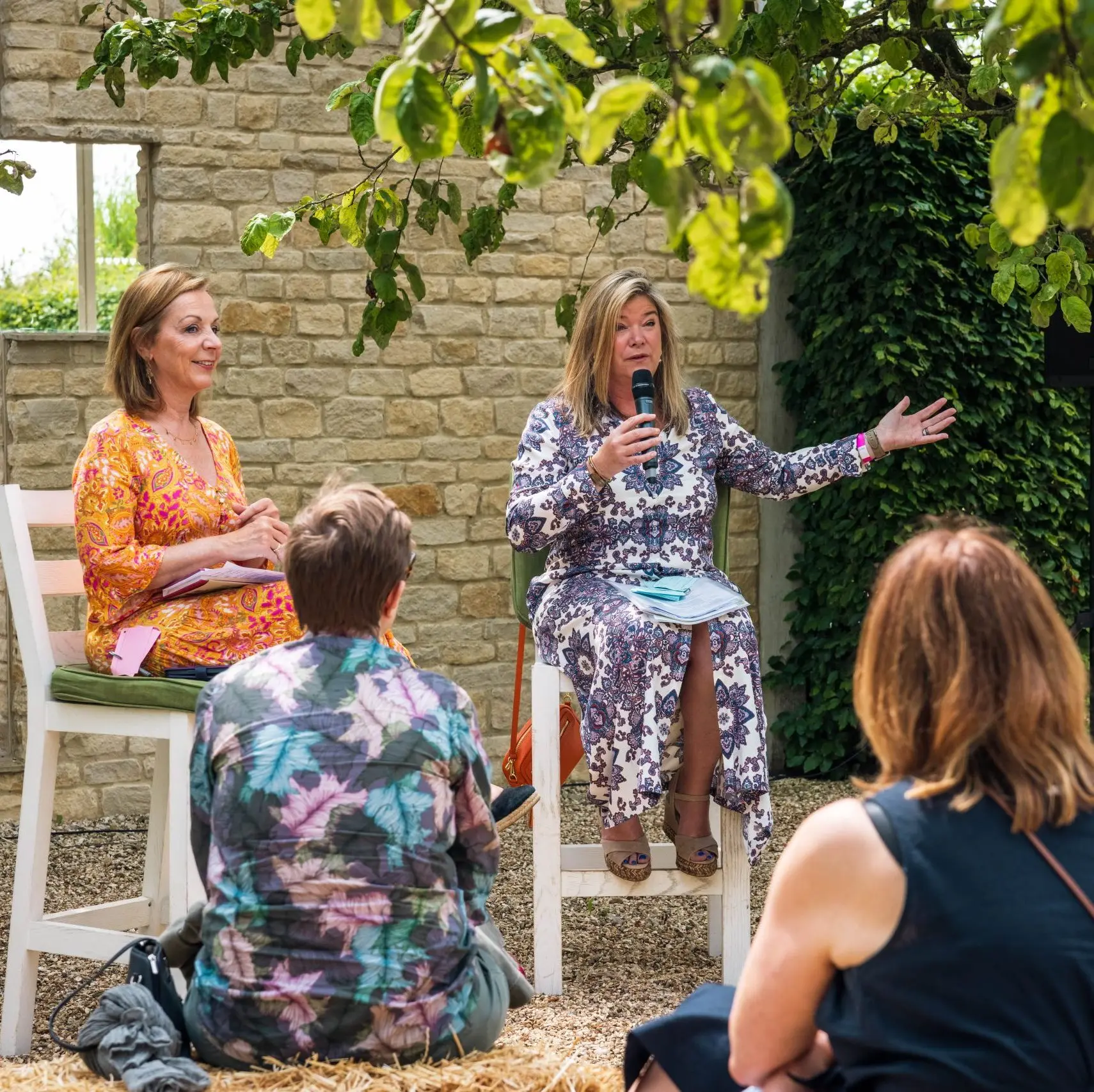 Two women outside on stools speaking to a crowd